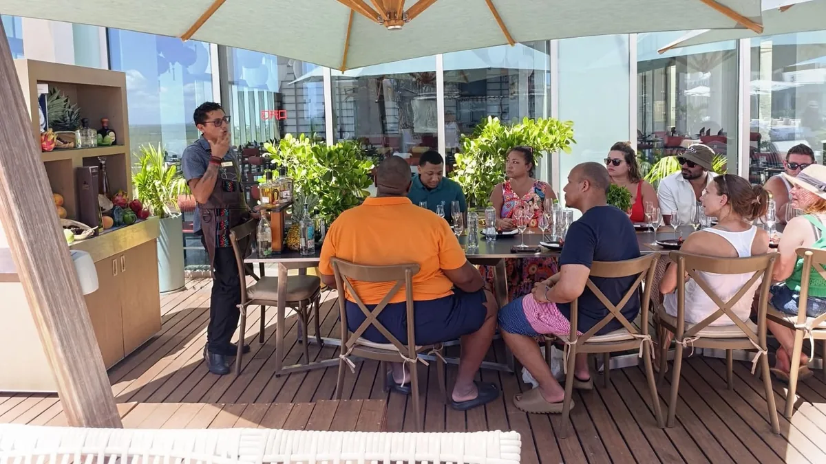 Una persona con mandil explica una degustación a un grupo sentado en una terraza bajo una sombrilla.
