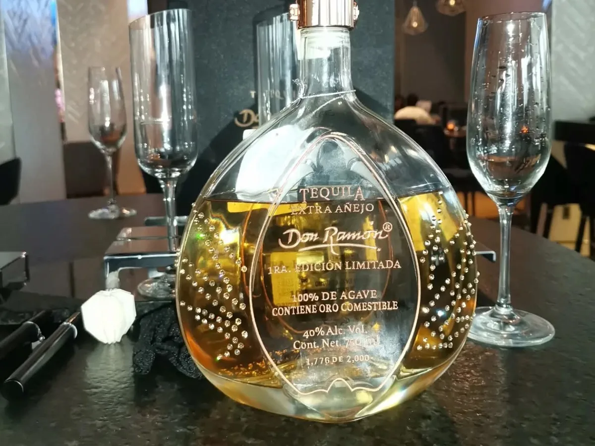 Botella redonda de tequila sobre una barra junto a copas vacías.